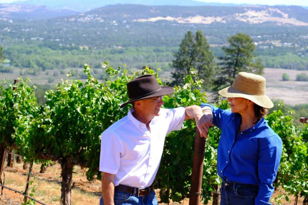 a man and a woman standing in a vineyard.